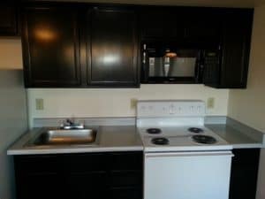 Kitchenette with dark wood finish, full size stove and microwave. - Emerald Suites Cameron